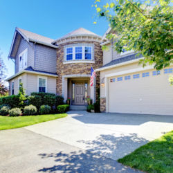 Beautiful American home exterior with stone tower and garage during summer.